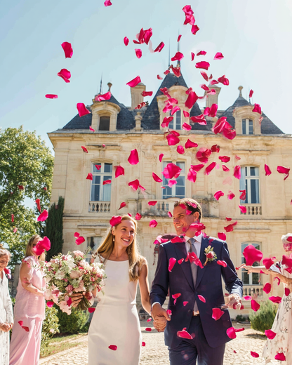Lancer de pétales de rose cerise foncé à la sortie des mariés devant un château | The Originea