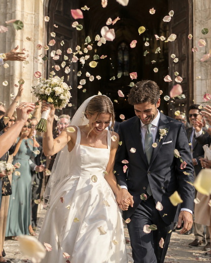 Lancer de confettis pétales rose et hortensia à la sortie d'église, mariés sous une pluie pastel | The Originea