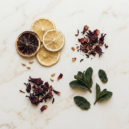 Agrumes séchés, hibiscus et menthe séchés disposés à plat sur marbre clair | The Originea