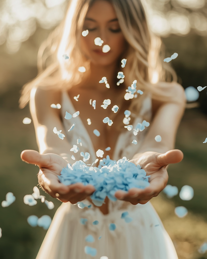 Mariée tenant des confettis d'hortensias bleu clair dans ses mains, pétales s'envolant au coucher du soleil