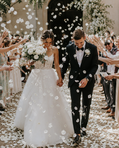 Couple de mariés sous une pluie de pétales de rose blanc séchés à la sortie de l'église — confettis mariage biodégradables The Originea