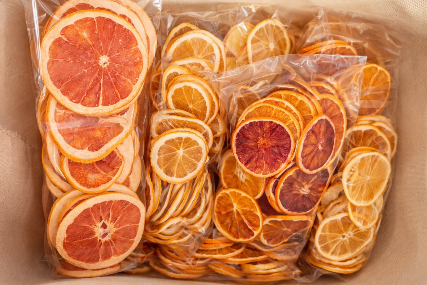 Vue du dessus de trois sachets transparents de tranches d'agrumes deshydratees : orange sanguine, citron et melange d'oranges dans une boite kraft