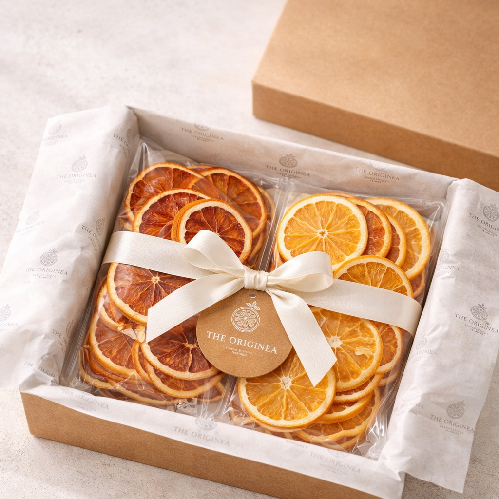 Coffret cadeau The Originea ouvert avec deux sachets de tranches d'oranges et d'oranges sanguines deshydratees noues d'un ruban satin creme sur papier de soie