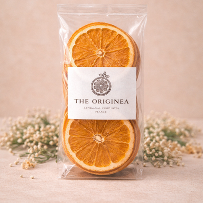 Sachet The Originea de tranches d'oranges deshydratees avec etiquette rectangulaire, entoure de fleurs de gypsophile sechees sur fond lin beige