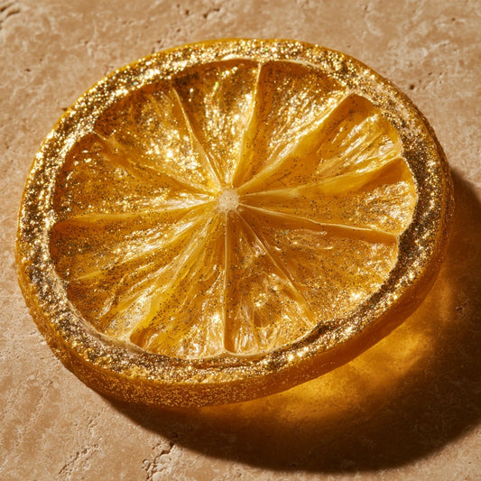 Tranche de citron jaune séchée entièrement dorée aux paillettes d'or, gros plan sur travertin | The Originea