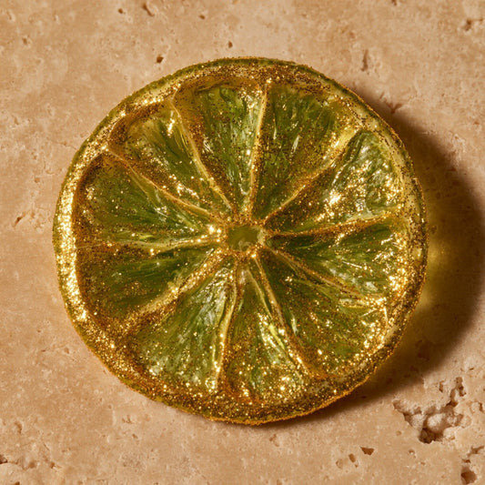 Tranche de citron vert séchée entièrement dorée aux paillettes d'or, gros plan sur travertin | The Originea
