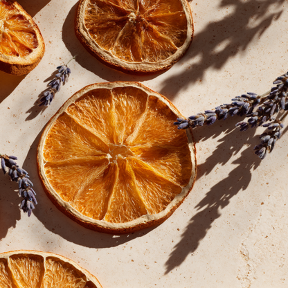 ranches d'oranges deshydratees avec brins de lavande sechee sur fond pierre beige en lumiere solaire rasante