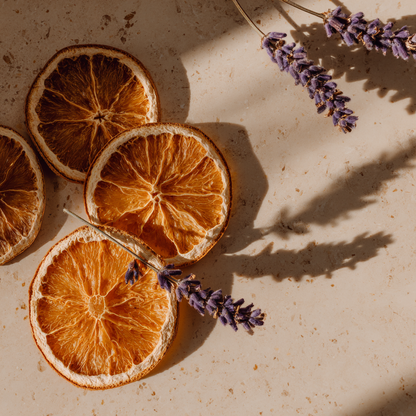 Trois tranches d'oranges deshydratees avec tiges de lavande sechee sur pierre beige en lumiere naturelle chaude