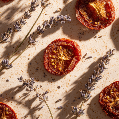Vue du dessus de tranches de tomates deshydratees et tiges de lavande sechee disposees sur fond pierre beige en lumiere naturelle